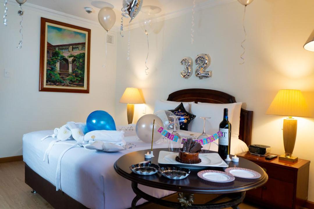Torre Monserrate Bogota Exterior photo The photo shows a decorated hotel room or a cozy setting for a celebration. In the room, there is a bed with white bedding, two lamps on either side, and a large artwork hanging on the wall. Balloons in various colors, including blue and silver, are 