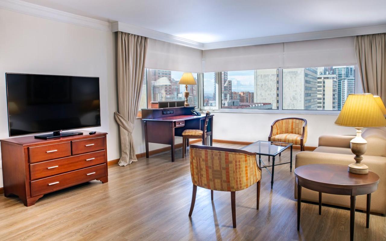 Torre Monserrate Bogota Exterior photo The photo shows a modern living space or hotel room with a cozy, contemporary design. 

- **Furniture**: There is a wooden TV stand with a flat-screen television mounted on the wall, a coffee table in the center, and two upholstered chairs around it.