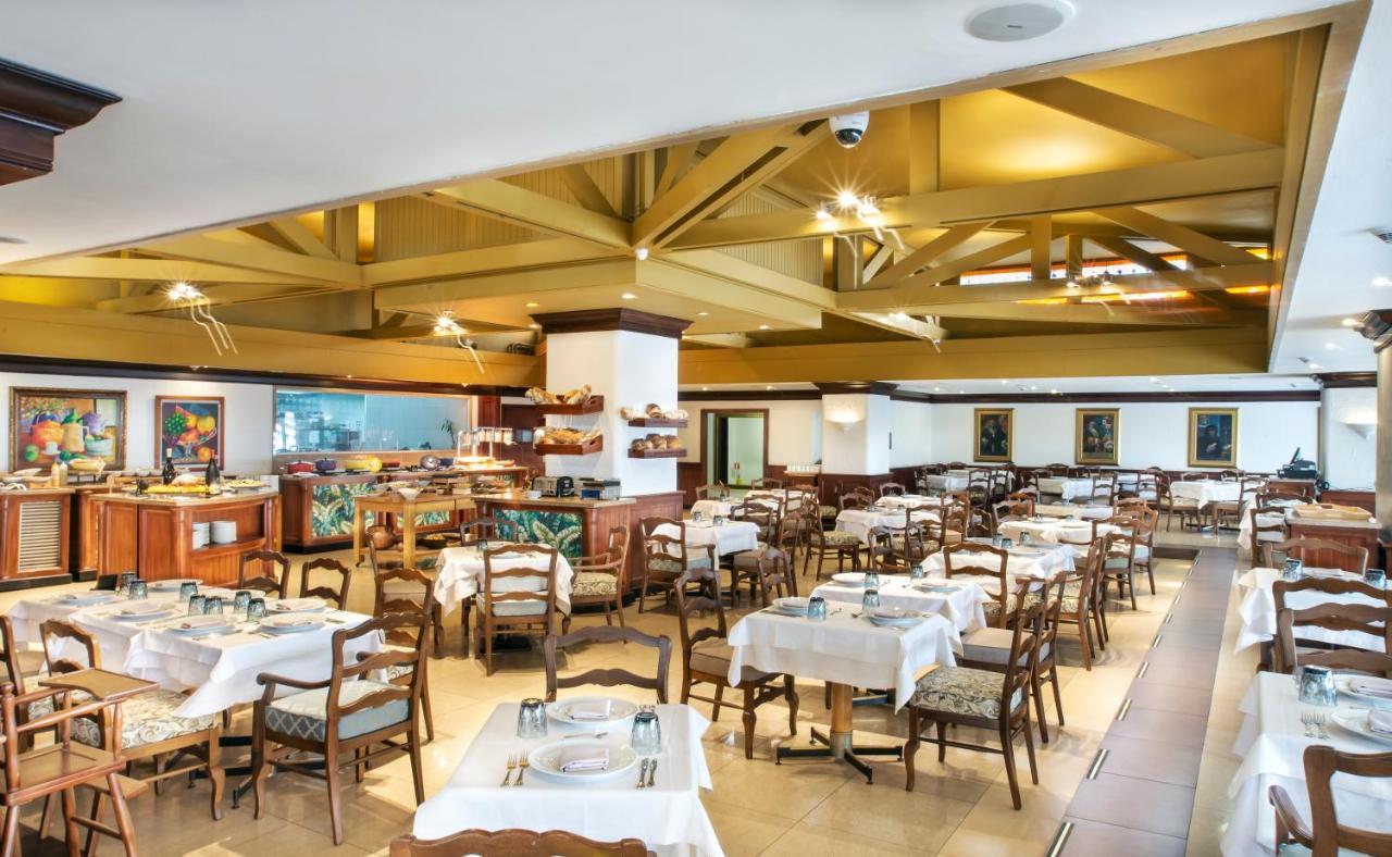 Torre Monserrate Bogota Exterior photo The photo shows the interior of a restaurant. It features a spacious dining area with several tables, each covered with white tablecloths and equipped with settings for diners. The ceiling has exposed beams, adding a rustic touch to the decor. There'