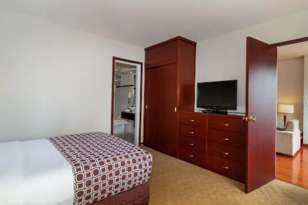 Torre Monserrate Bogota Exterior photo The photo depicts a bedroom. On the left, there is a bed with a patterned bedspread featuring a geometric design in shades of brown and white. Next to the bed, there's a wooden cabinet or dresser, likely containing storage for clothes and personal it