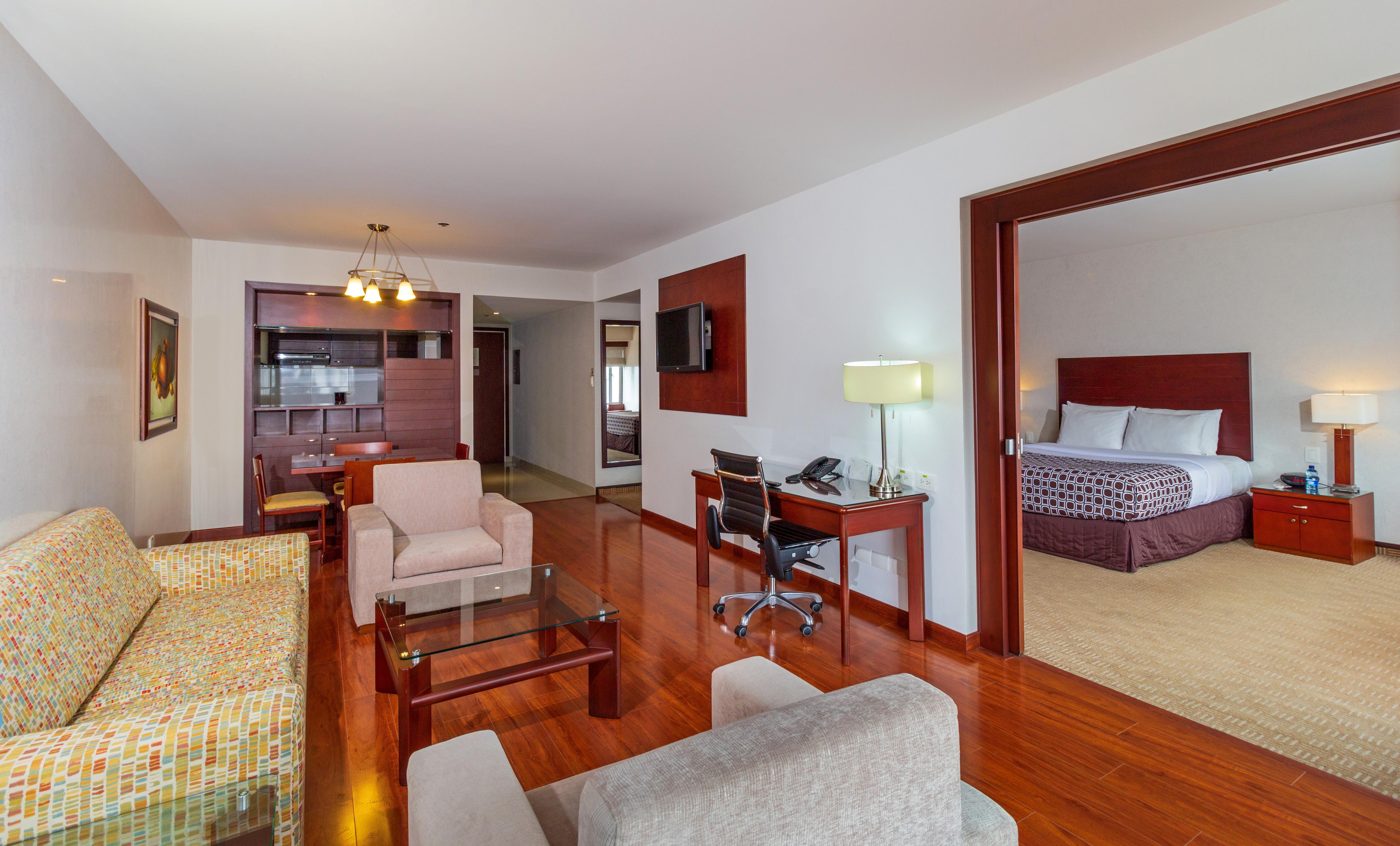 Torre Monserrate Bogota Exterior photo The photo shows a hotel suite or a spacious living area. The room features hardwood floors and a layout that includes a seating area with two armchairs and a small table, along with a colorful sofa. There's a work desk with a chair, a television moun
