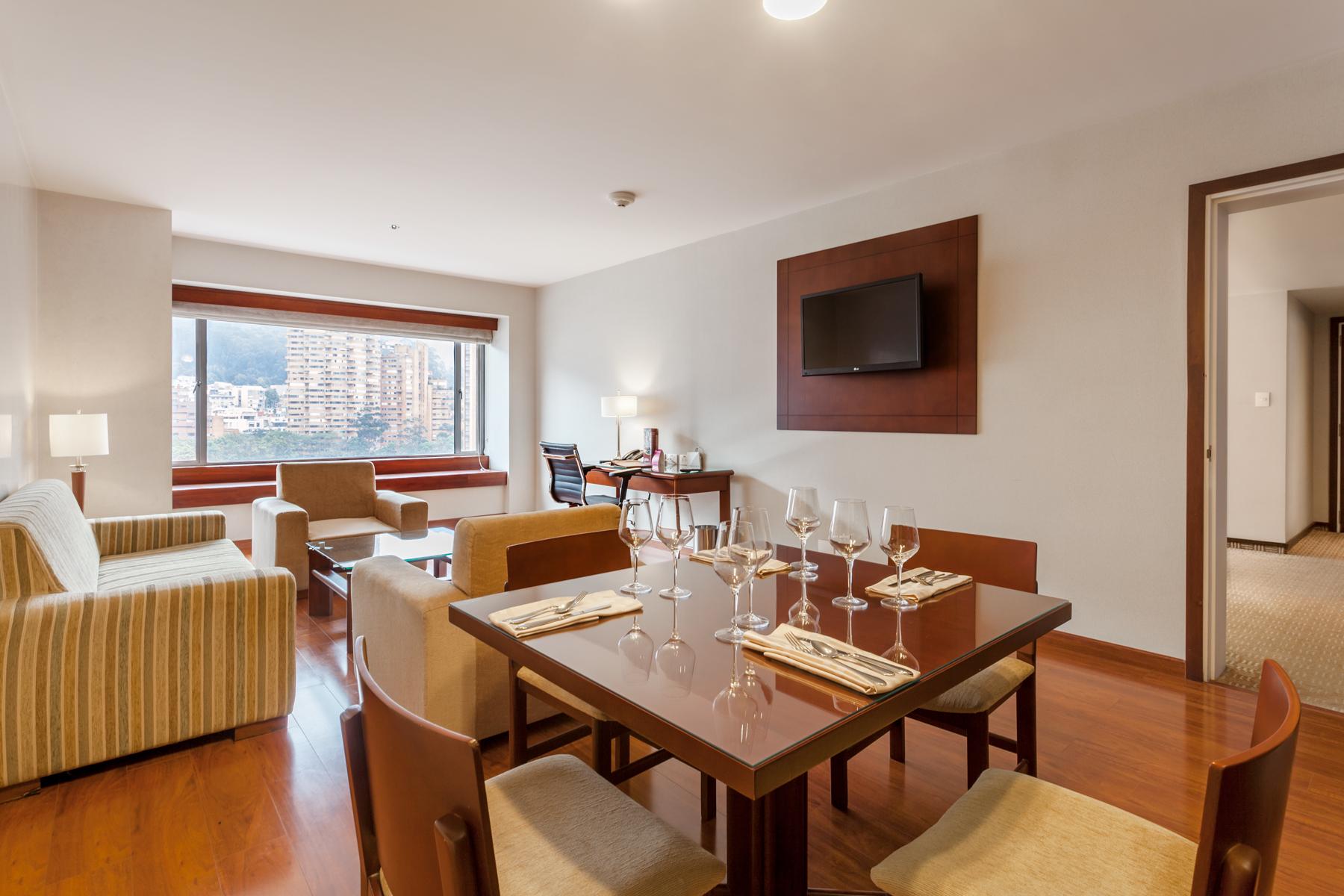 Torre Monserrate Bogota Exterior photo The photo shows a modern living space, likely a hotel suite or an apartment. It features a dining table set for several people, with glasses on the table. There is a comfortable seating area with a sofa and chairs, and a flat-screen TV mounted on the