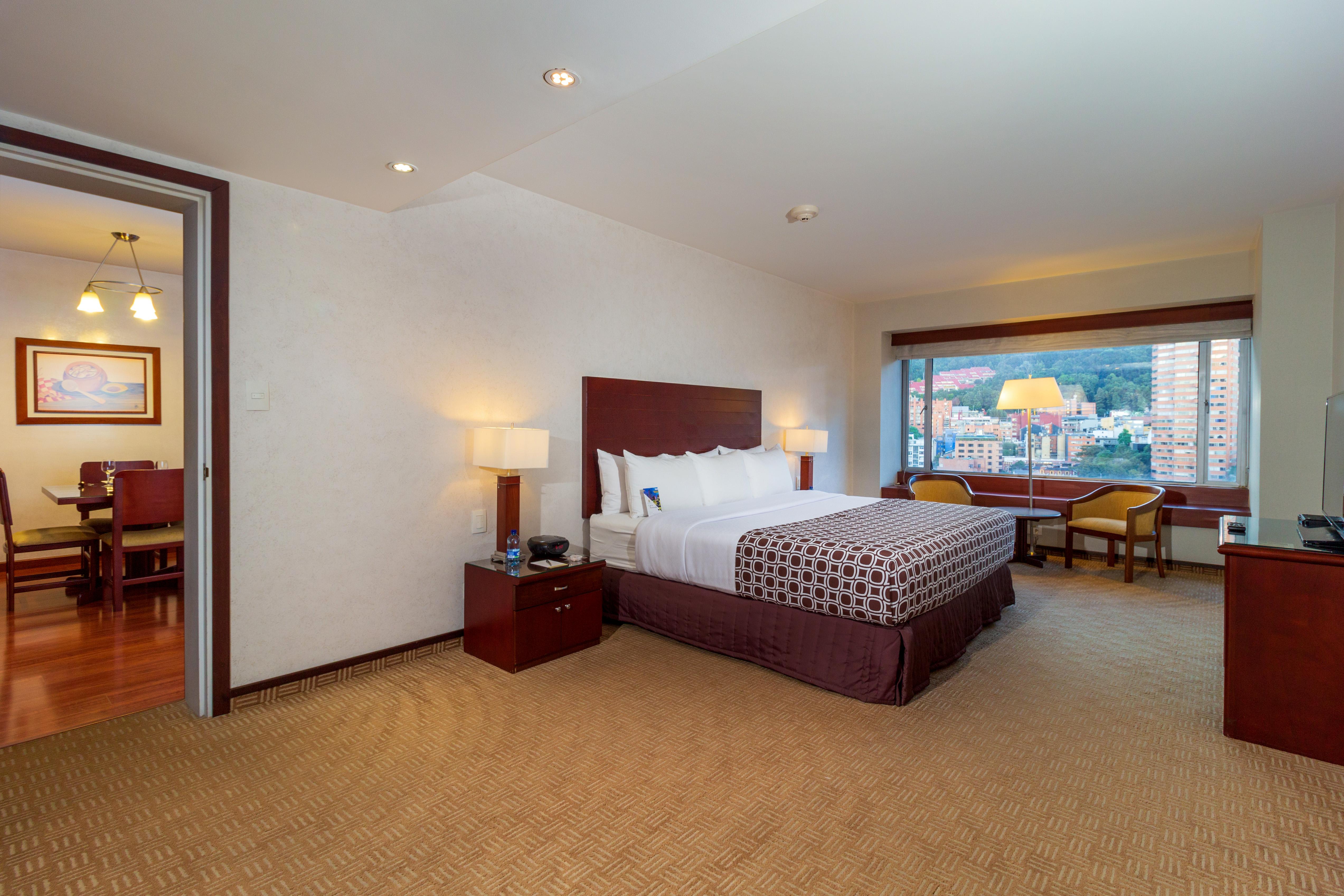 Torre Monserrate Bogota Exterior photo The image shows a hotel room with a modern design. It features a large bed with decorative pillows, positioned against a dark wooden headboard. On either side of the bed, there are bedside tables with lamps. The room has a warm color palette and is w