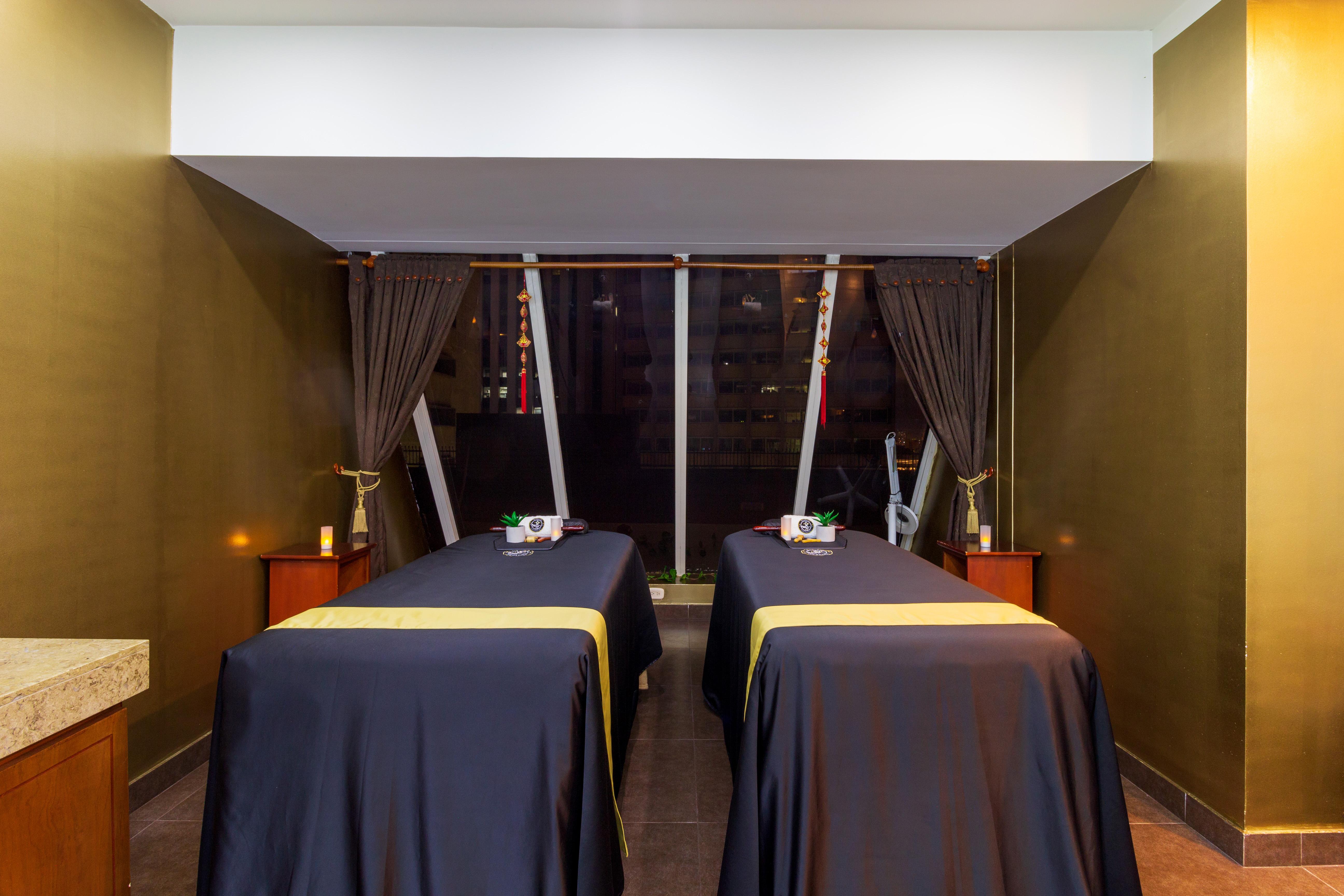 Torre Monserrate Bogota Exterior photo The photo shows a spa treatment room featuring two massage tables covered with dark blue cloths. Each table is set with small towels or accessories on top. The walls are painted a deep green, and large windows with curtains allow for natural light. T