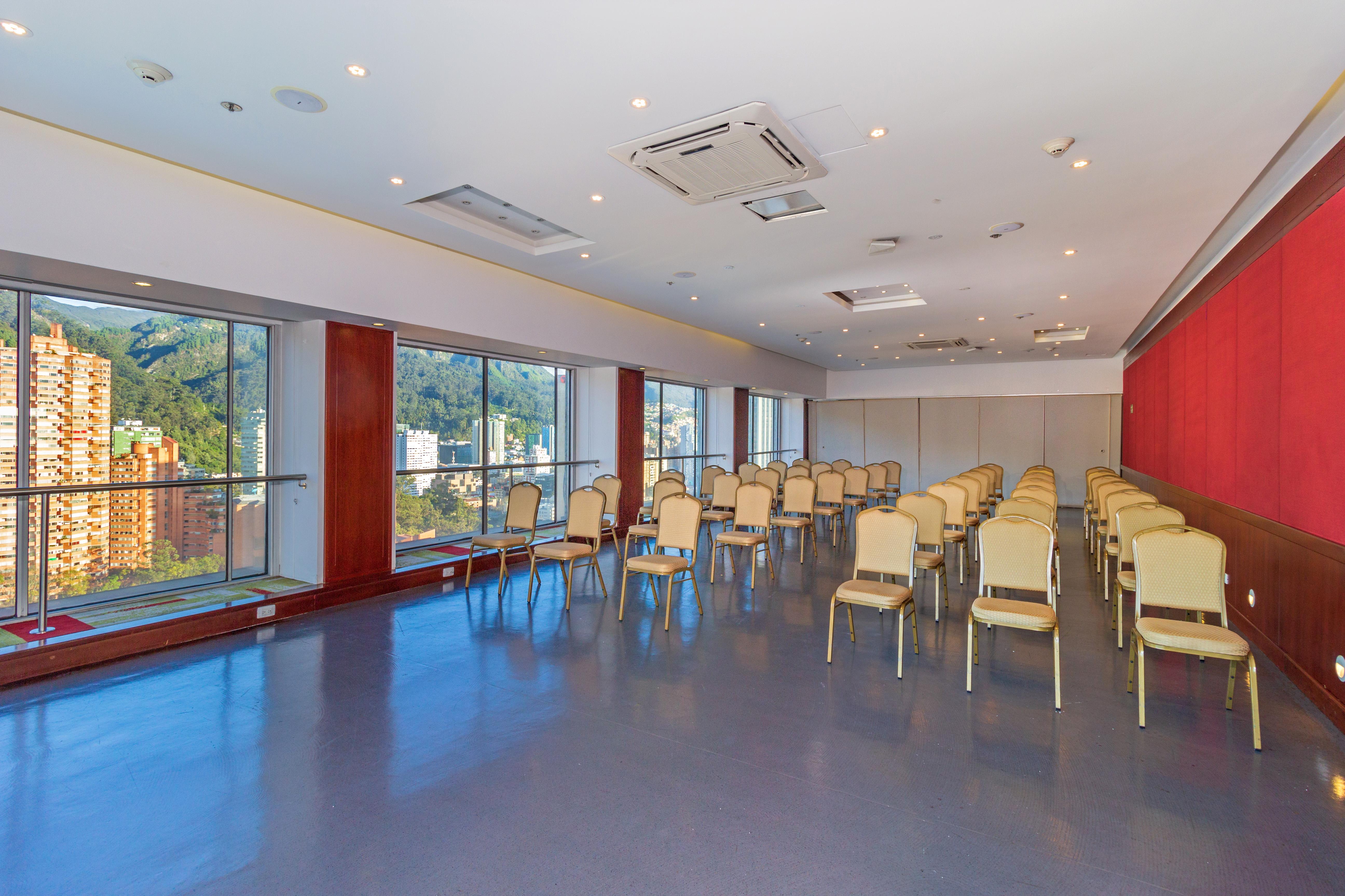 Torre Monserrate Bogota Exterior photo The photo shows a meeting or conference room with a modern design. It features several rows of beige chairs arranged neatly in front of large windows that provide natural light and a view of the outdoors. The walls have a combination of light colors,