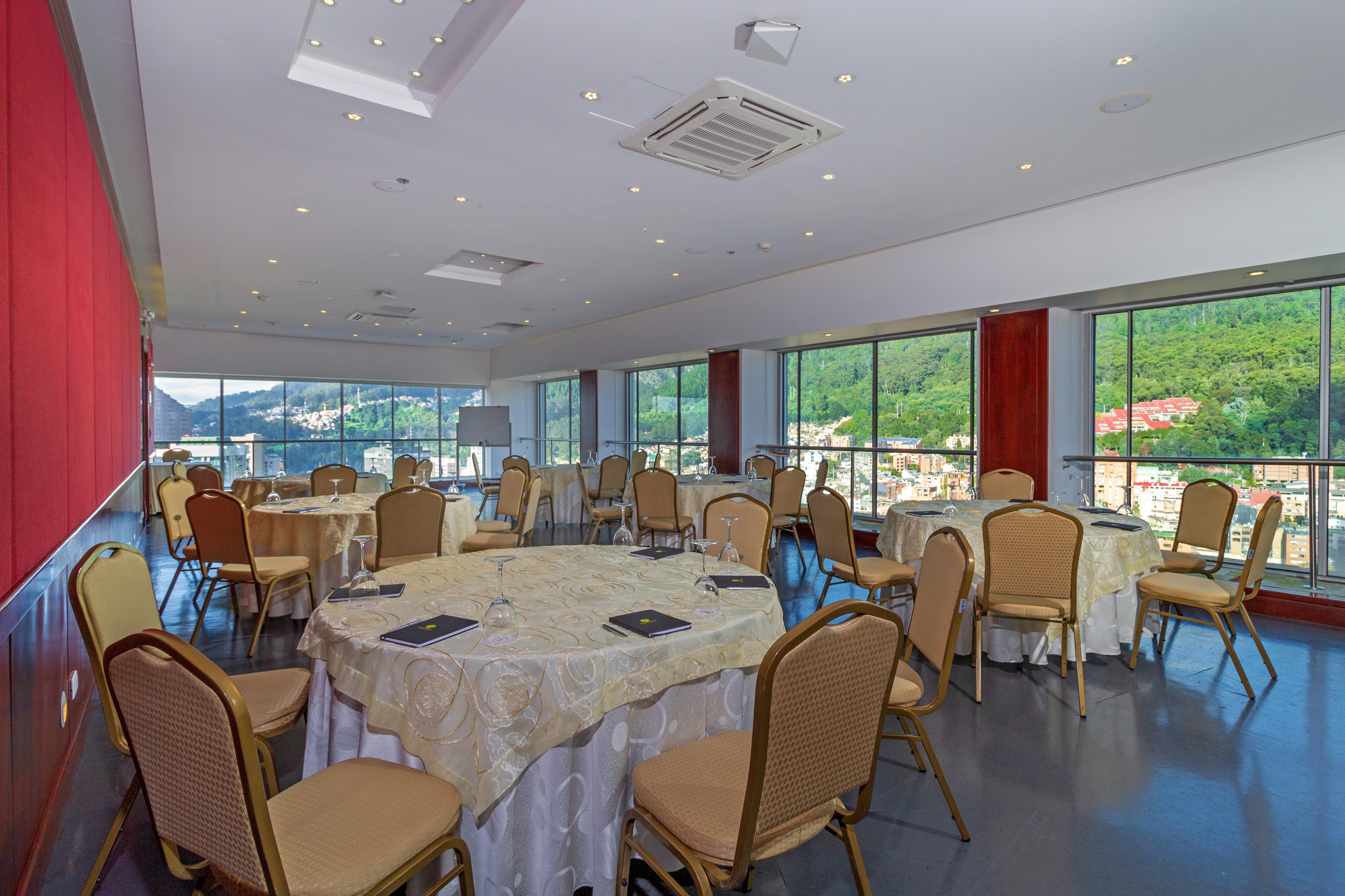 Torre Monserrate Bogota Exterior photo The photo depicts a spacious and elegantly designed meeting room or banquet hall. It features several round tables covered with white tablecloths, each accompanied by beige chairs. The room has large windows that allow natural light to flood in, offe