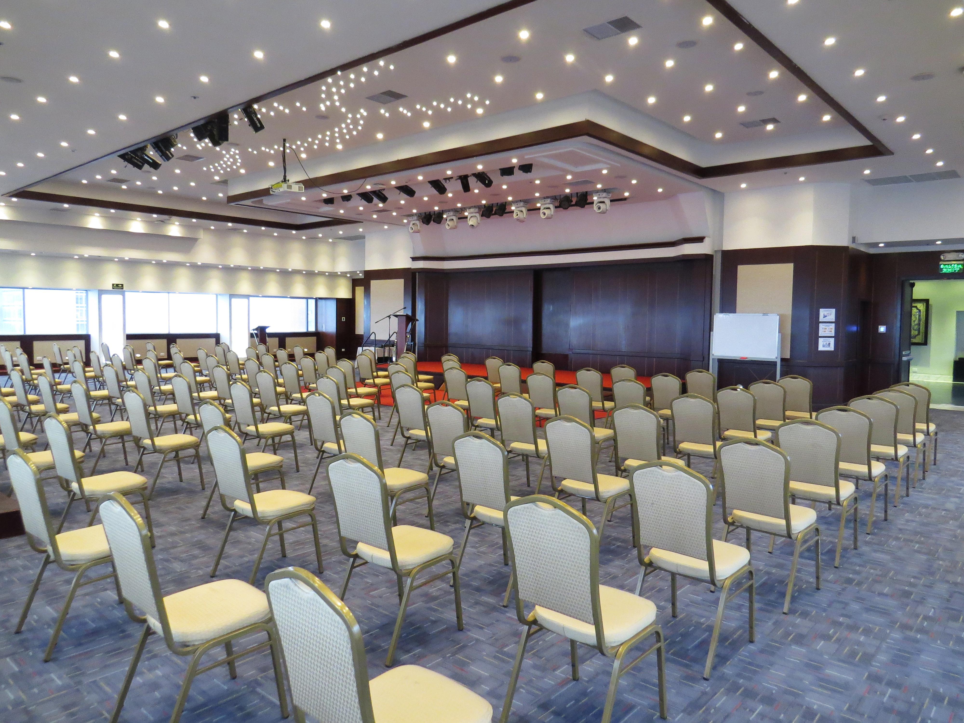 Torre Monserrate Bogota Exterior photo The photo shows a spacious conference or event room set up with numerous empty chairs arranged in rows. The chairs are light-colored with gold accents. The room features a modern design with a high ceiling, decorated with lights that give it a bright