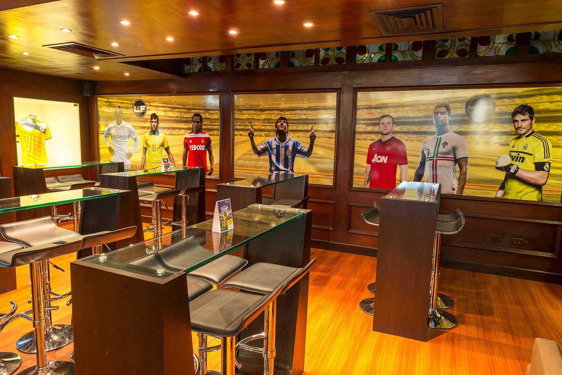Torre Monserrate Bogota Exterior photo The photo shows a modern sports bar or lounge with a stylish interior. There are high tables with bar stools arranged around the space. On the walls, there are large murals depicting male athletes in soccer jerseys from various teams, celebrating or 