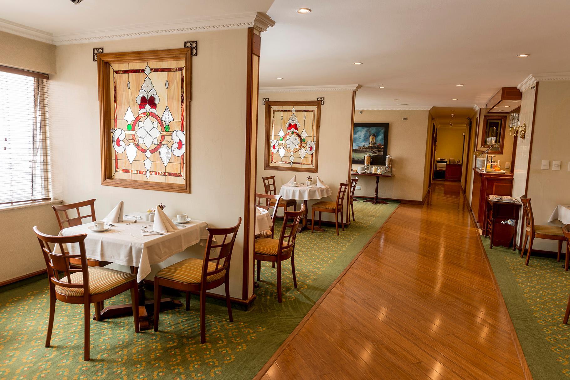 Torre Monserrate Bogota Exterior photo The photo shows an interior view of a restaurant or dining area. There are two tables set for dining, each with white tablecloths and chairs around them. The walls feature stained glass decorations, adding a decorative touch to the space. The floorin