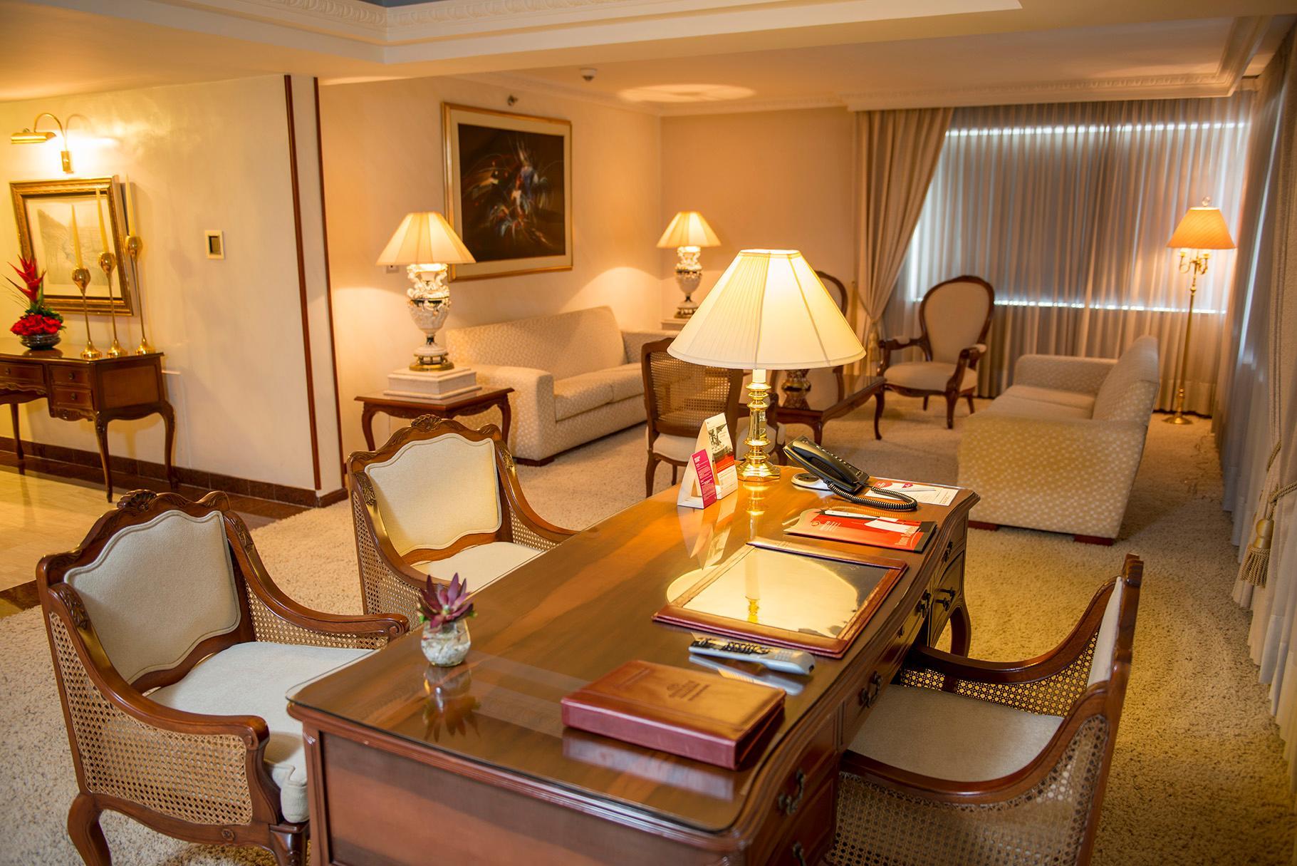 Torre Monserrate Bogota Exterior photo The photo depicts a well-furnished living room or office space. There are elegant pieces of furniture, including a wooden desk with decorative items and stationery on it. Seated around the desk are several upholstered chairs with light-colored fabric