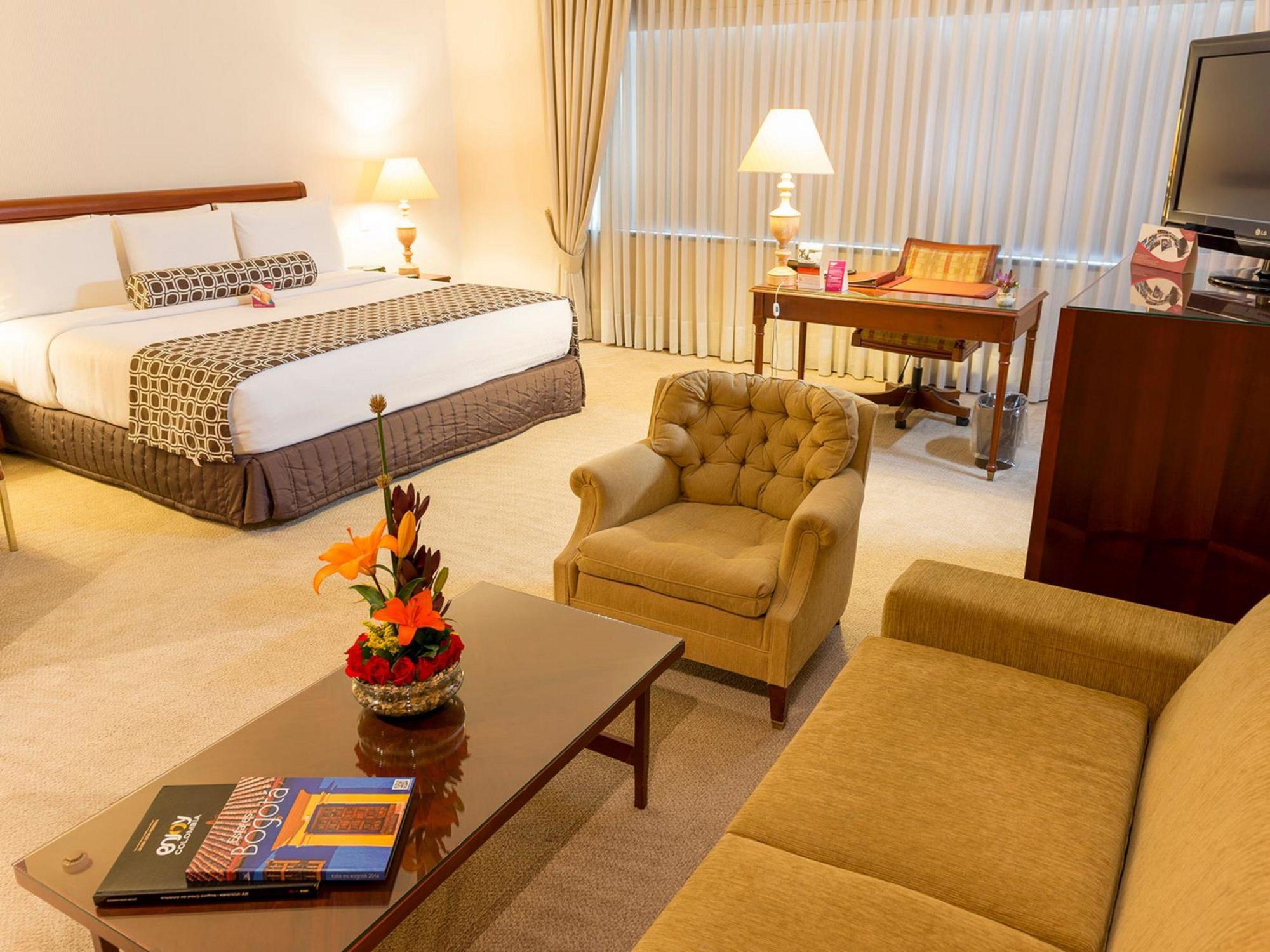 Torre Monserrate Bogota Exterior photo The photo depicts a well-furnished hotel room featuring a large bed with a patterned bedspread. There are bedside lamps on each side of the bed, and the room is decorated with soft, neutral colors. In the foreground, there's a coffee table with a sma